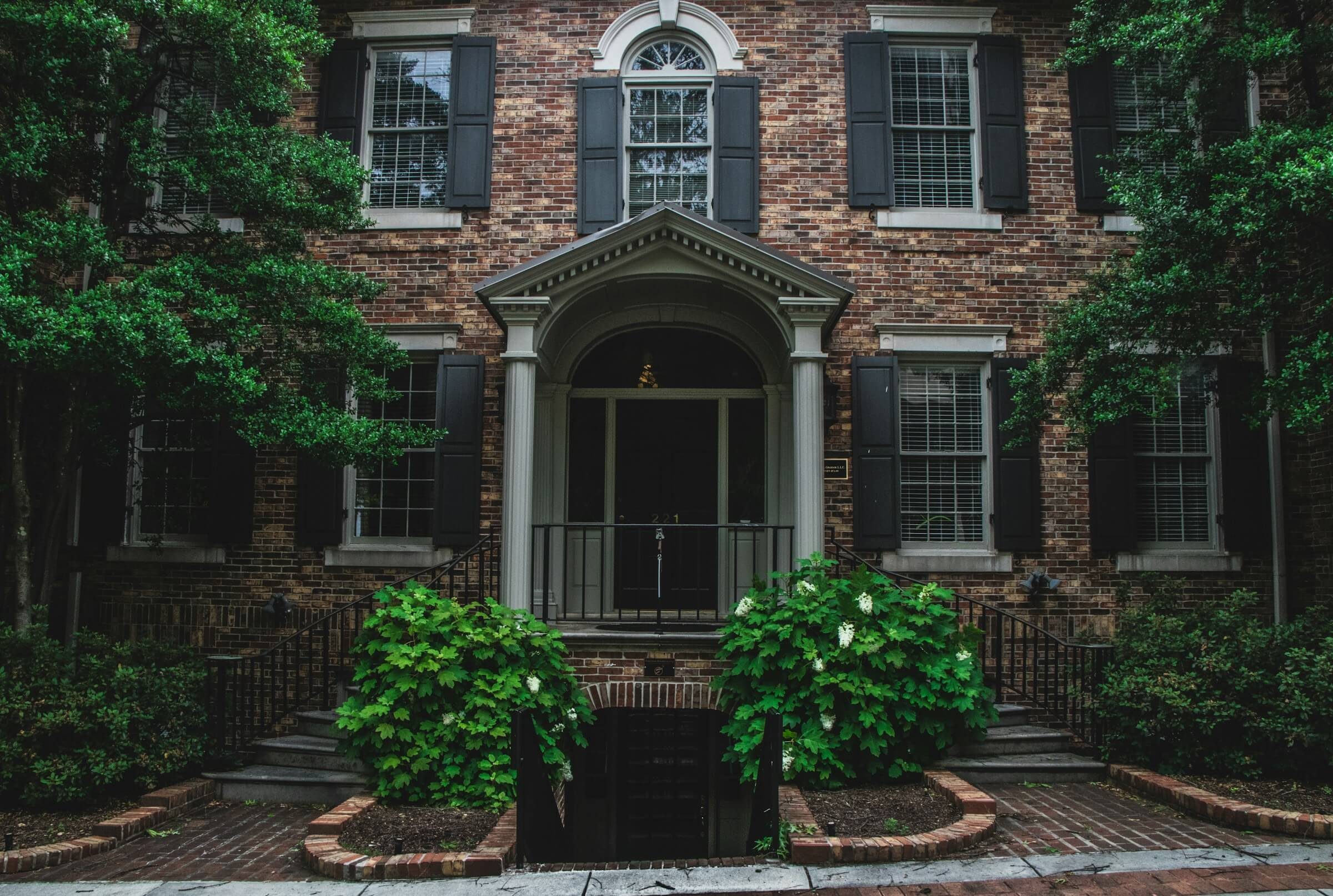 A brick Georgian house behind mature planting